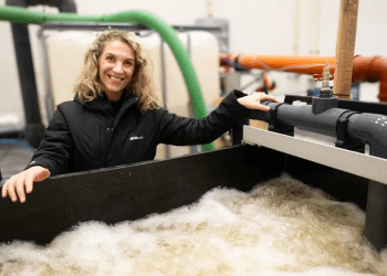 Siri Tømmerås de AKVA group se encuentra junto al mini desgasificador de CO₂, utilizado para probar cómo factores como la alcalinidad, el pH, la salinidad y la temperatura afectan la eficiencia de la desgasificación. Créditos: AKVA group.