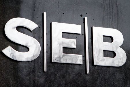 Logotipo de SEB en letras metálicas sobre una pared oscura.